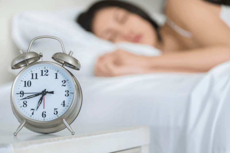 woman sleeping in bed in background, alarm clock in the foreground