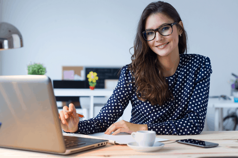 smiling woman sitting at desk with laptop and cup of coffee